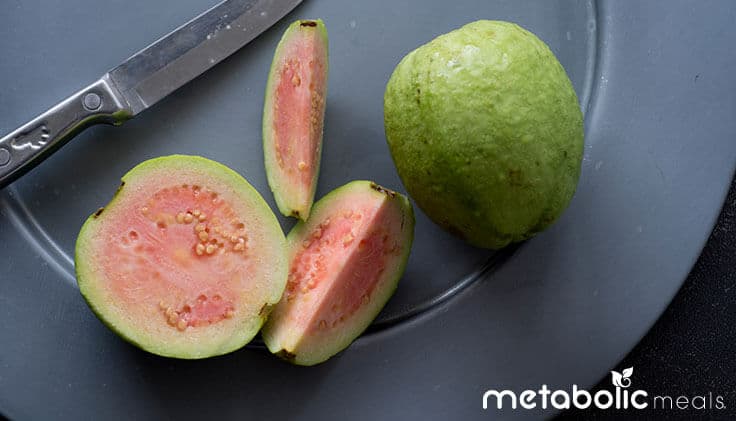 Sliced and whole guava on cutting board with knife.